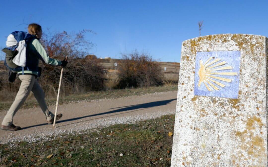 Pauline marchant sur une route avec son bâton de pèlerine devant une borne du chemin de compostelle