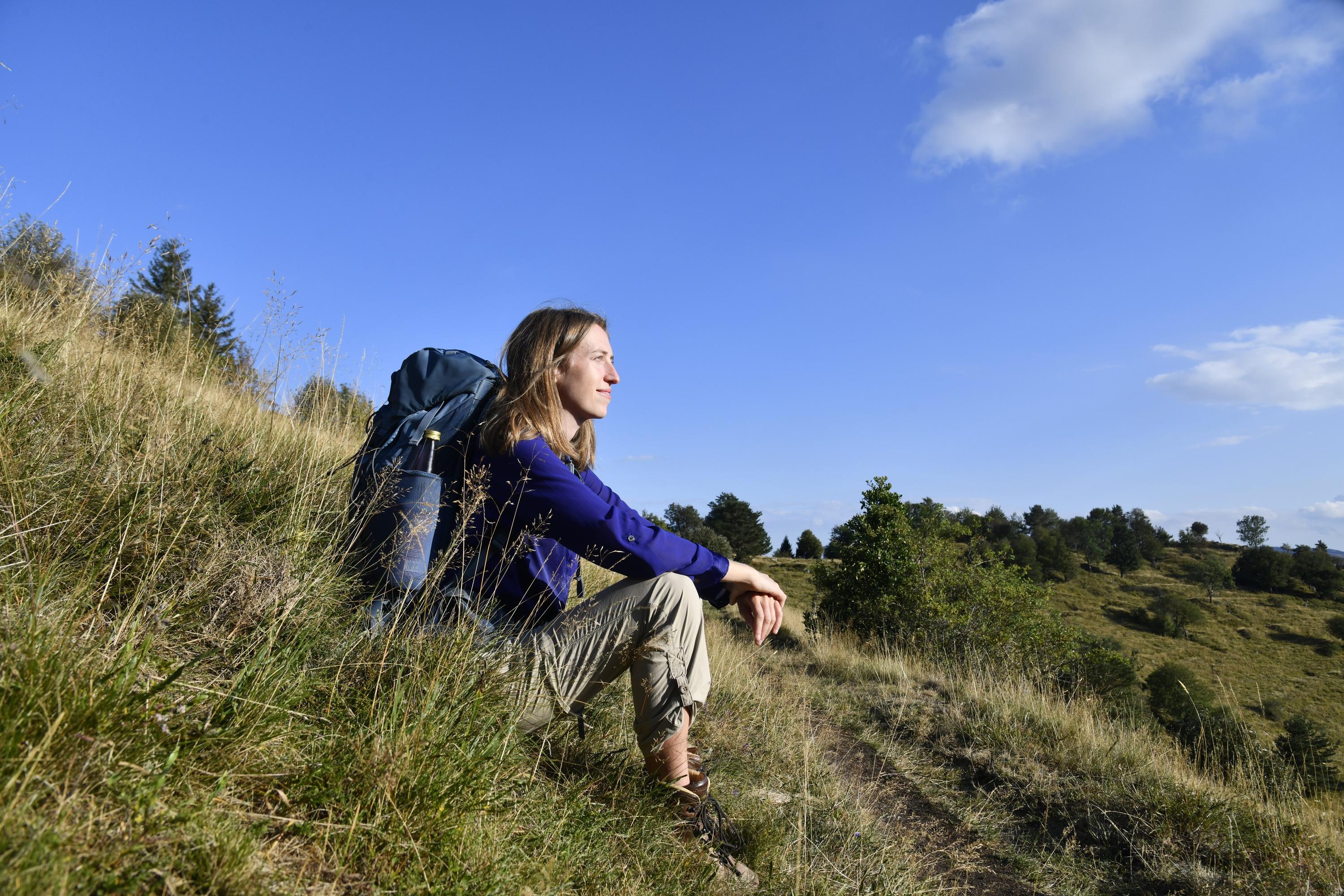 Pauline assise dans l'herbe avec un sac à dos sur le dos